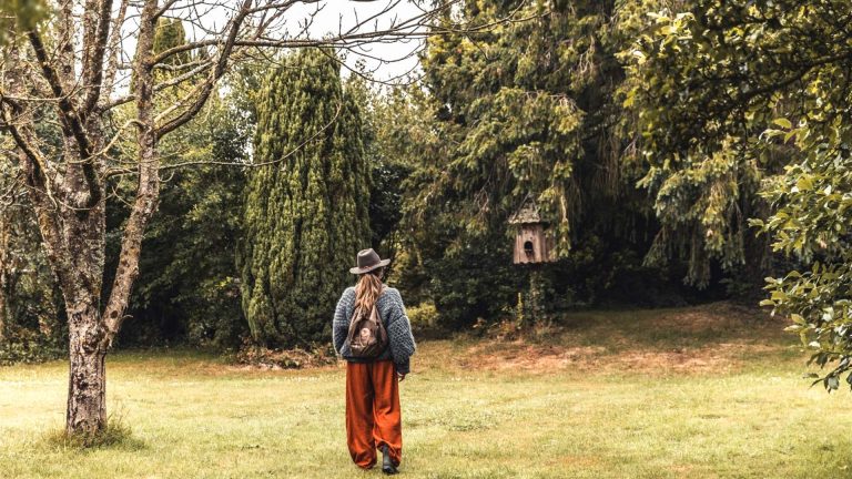 Woman walking across a grassy campsite in Normandy towards tall trees and a dovecote.