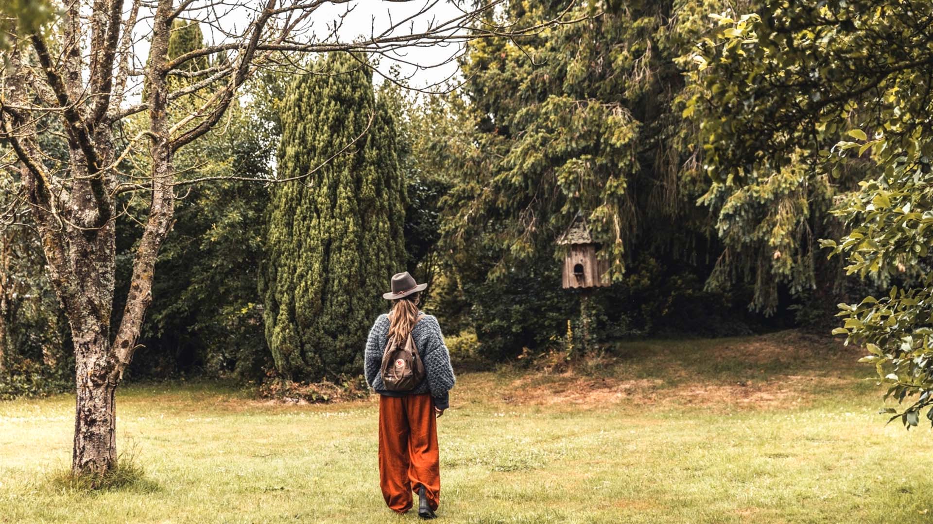 Woman walking across a grassy campsite in Normandy towards tall trees and a dovecote.